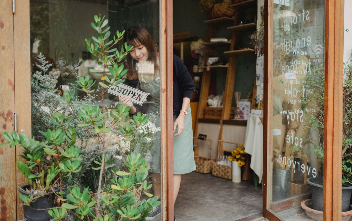 A shop owner turning an open sign in the glass door of a plant shop