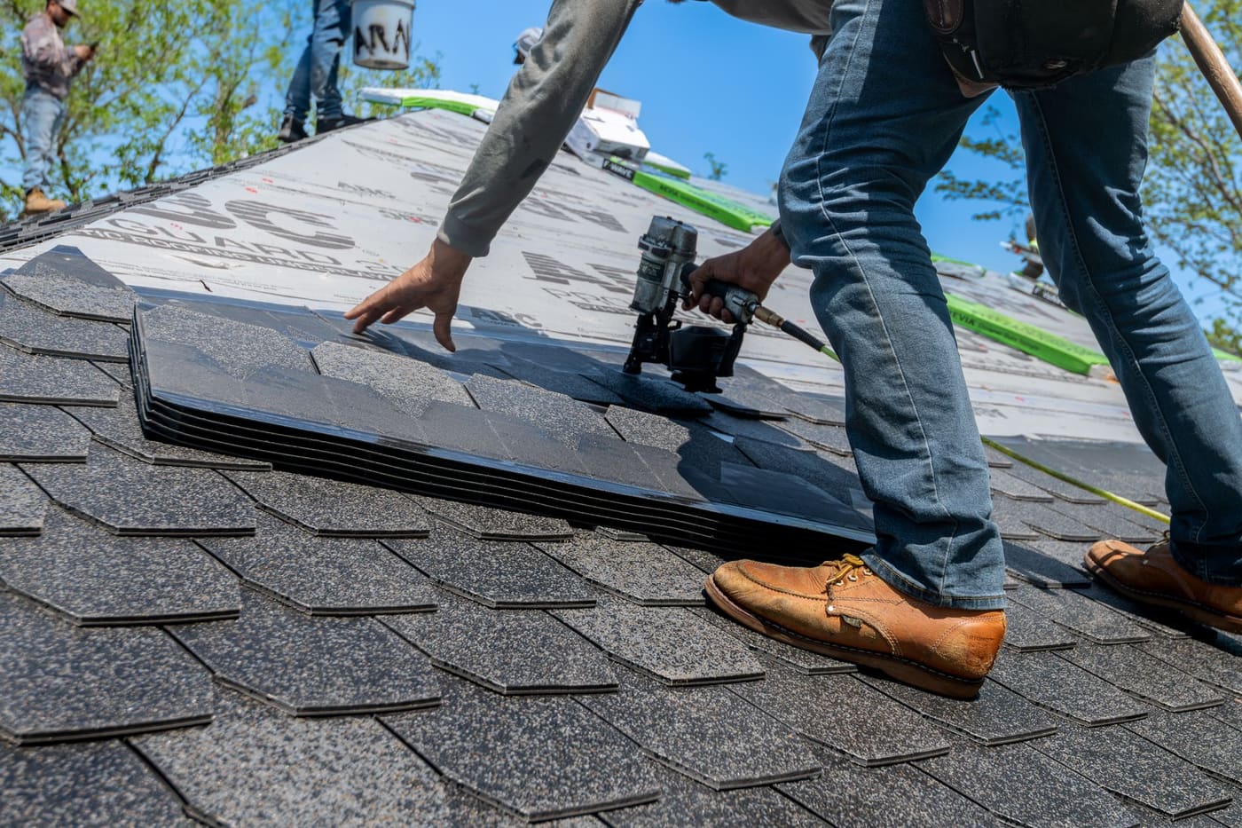 A roofer using a nail gun to fix shingles on a house roof