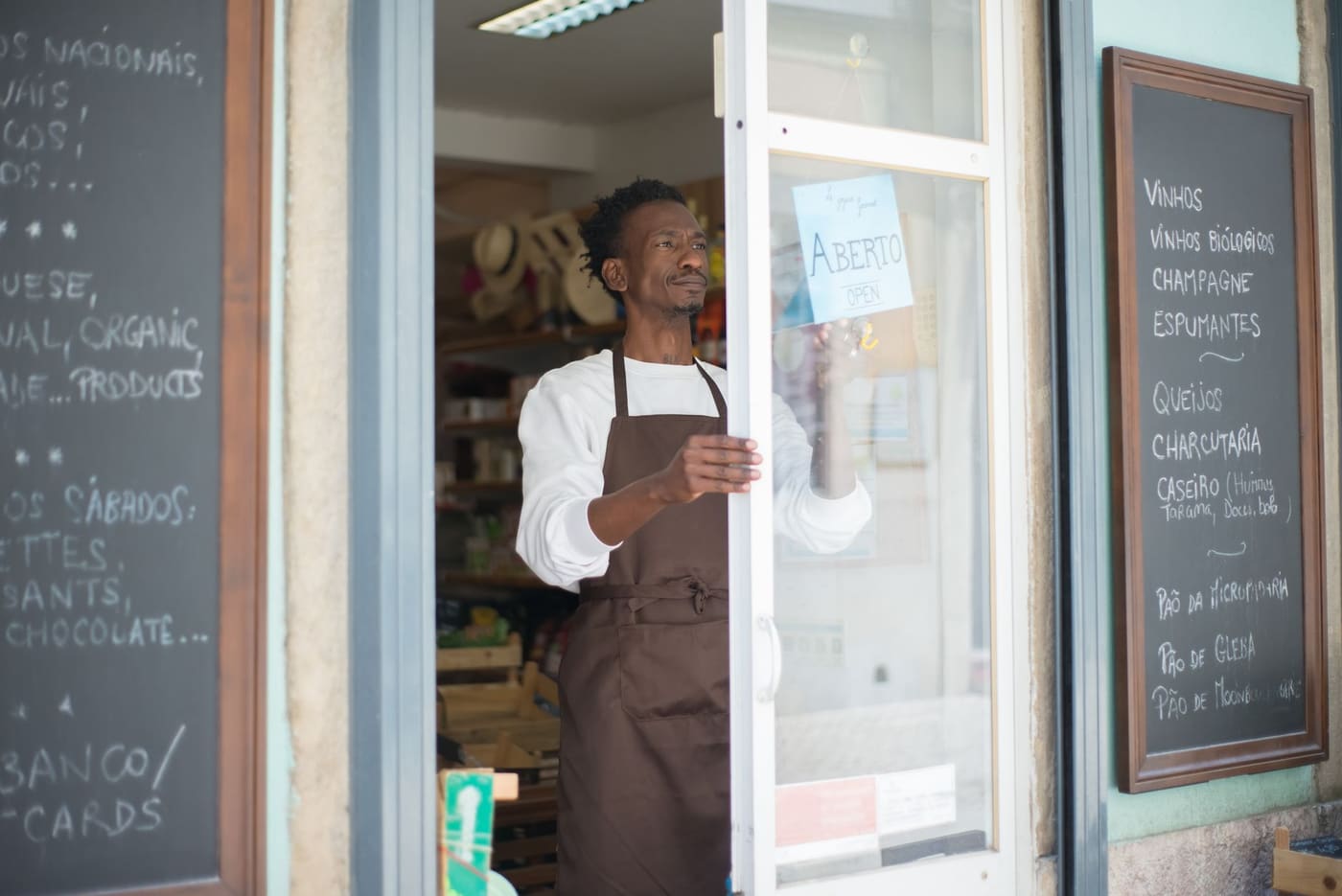 A shop owner in an apron opening the glass door of a small grocery store
