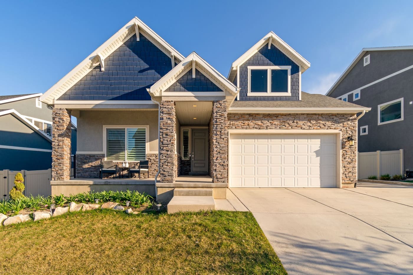 A suburban home with a stone facade, garage and neat lawn under a blue sky