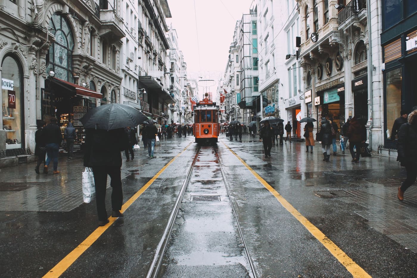 A tram on a wet street with pedestrians carrying umbrellas